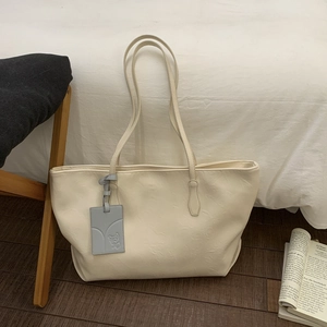 Detailed view of cream white tote bag with gray embossed leather charm and shoulder straps