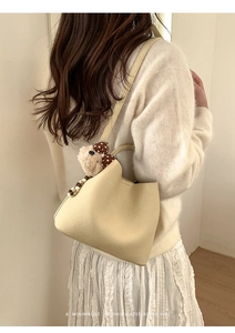 Chic cream bucket bag with plush bear charm shown on model for size and style reference