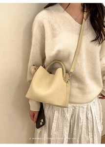 Close-up of minimalist cream bucket bag with wavy edge and荔枝 texture on model