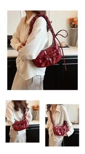 Detail of red pleated half-moon shoulder bag with bow and ruffled cloud-like strap