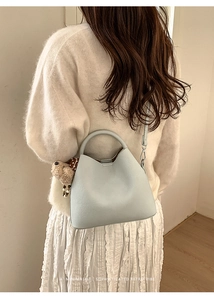 Minimalist light blue bucket bag with leather texture shown on model's shoulder
