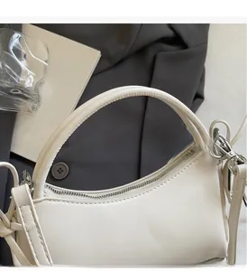 Detail der cremeweißen PU-Leder-Handtasche mit Reißverschluss und Metallschnalle auf Anzug
