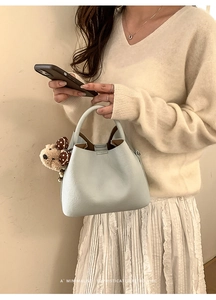 Detail of light blue pebble leather bucket bag with a cute brown plush bear charm