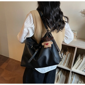 Detail of black tote bag with leather texture and cute bear pendant on model back