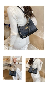 Close-up of dark blue denim underarm bag featuring a gold buckle and chunky metal chain