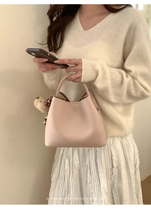 Detail view of beige bucket bag with lychee texture and cute bear pendant charm