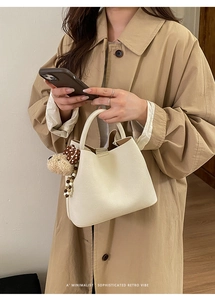 Detail of minimalist cream leather bucket bag with cute plush puppy charm accessory