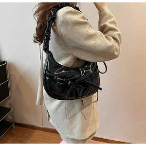 Detail of black patent leather hobo bag featuring pleated textures and a bow accent
