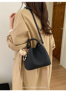 Detail of black leather bucket bag with plush bear charm worn with beige coat