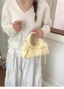 Close-up of beige handbag featuring decorative bow knots and soft pleat details