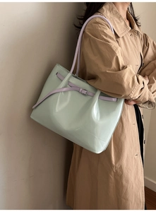 Detail of high-gloss mint green tote bag with purple straps on model in trench coat