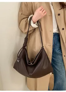 Close-up of deep brown leather tote bag with unique twisted strap and brand tag detail