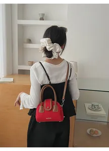 Detailed view of red mini Boston bag with brown handles and elegant crossbody leather strap