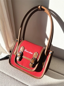 Detail shot of a red canvas handbag with brown leather trim and silver metal buckles