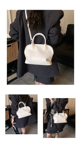 Detail view of off-white leather shell bag showing top handles and adjustable shoulder strap