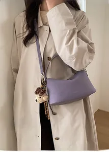Dettaglio borsa a mezzaluna viola chiaro con peluche cane leopardato su un trench beige