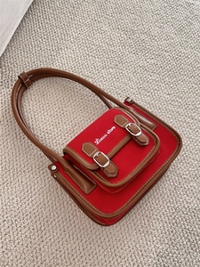 Close-up of red canvas bag with brown leather trim and white stitching detail