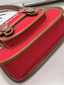 Detail of red canvas underarm bag with brown leather trim and white embroidered text