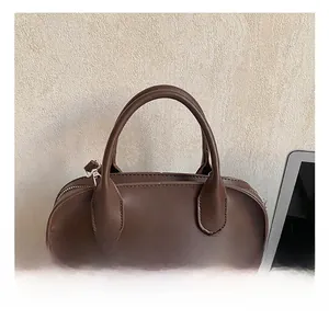 Detail of dark brown leather handbag featuring rounded top handles and silver zipper puller