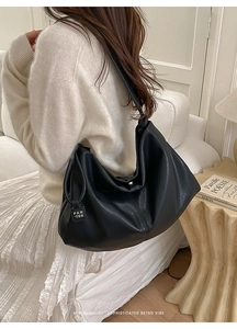 Close-up of a large black leather tote bag with a brand tag, styled on a shoulder