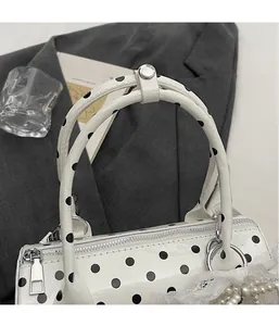 Detailed close-up of white polka dot boston bag with pearl lace charm and silver hardware