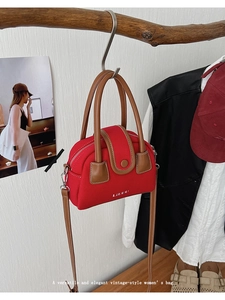 Close-up of red vintage-style handbag with leather trim hanging on a wooden branch