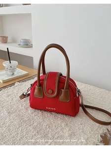 Detail of red canvas crossbody bag with brown leather handles and brand logo
