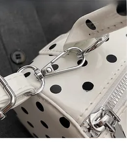 Detailed close-up of silver metal hooks and hardware on a white polka dot barrel bag