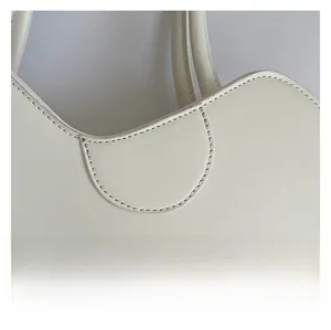 Close-up of premium creamy white leather texture and precise curved stitching on bag