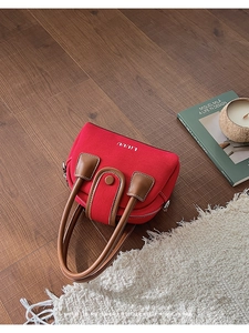 Top-down view of a red canvas handbag with brown leather handles on a dark wood floor