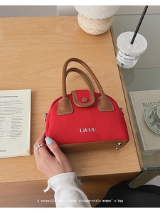 Detail of red canvas tote with leather trim, base studs and embroidered logo on wood table