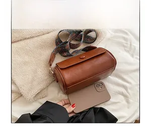 Brown leather cylinder bag size comparison with smartphone and boho embroidered strap