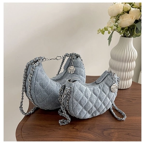 Detail der blauen Denim-Halbmondtaschen mit Rautensteppung und floralem Kettenanhänger