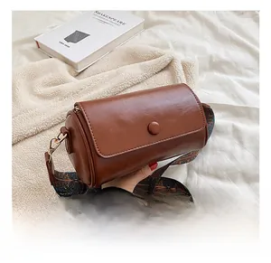 Detail view of brown cylinder bag with ethnic patterned wide strap on a soft white bed
