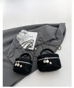 Detail of quilted black mini bag with chain strap and flower charm on grey background