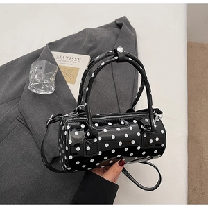 Detailed close-up of a black polka dot cylinder bag with glossy finish and top handles