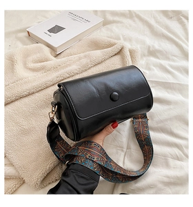 Close-up of black cylinder bag with vintage patterned wide strap on a soft blanket