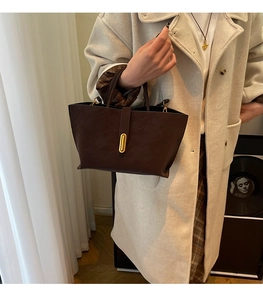 Close-up of deep brown matte leather tote with oval gold buckle and handle details