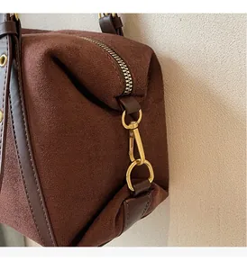 Detail of high-gloss gold hardware and matte brown suede texture on shoulder bag