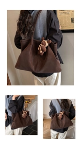 Detail of dark brown suede tote bag featuring white stitching and a cute bear charm