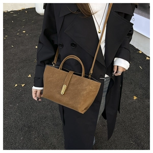 Top view of brown suede crossbody bag with gold buckle on a model in autumn street scene