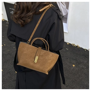 Close-up of a brown suede bucket bag with gold buckle on a model in street style setting