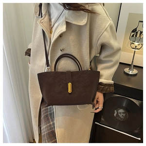 Detail of a dark brown faux leather handbag featuring a minimalist gold oval metal clasp