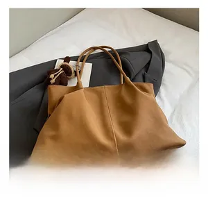Detail of a large brown faux suede tote bag with a cute knit bear charm on a grey suit