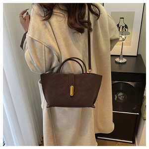 Deep brown matte leather tote bag with gold buckle shown on shoulder in a vintage setting