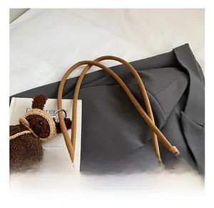 Detail of thin round handles on brown leather tote bag with knitted bear pendant