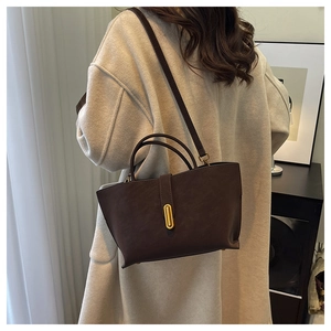 Close-up of matte dark brown handbag with gold oval buckle on white wool coat