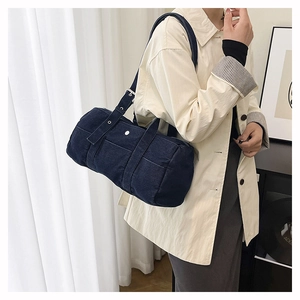 Detail of dark blue denim barrel bag with contrast white stitching and silver hardware
