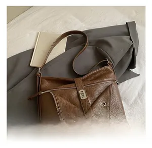 Close-up of brown litchi leather tote bag featuring double zippers and metallic buckle detail