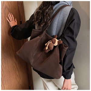 Detailed back view of a large brown matte tote bag with contrast stitching and bear charm